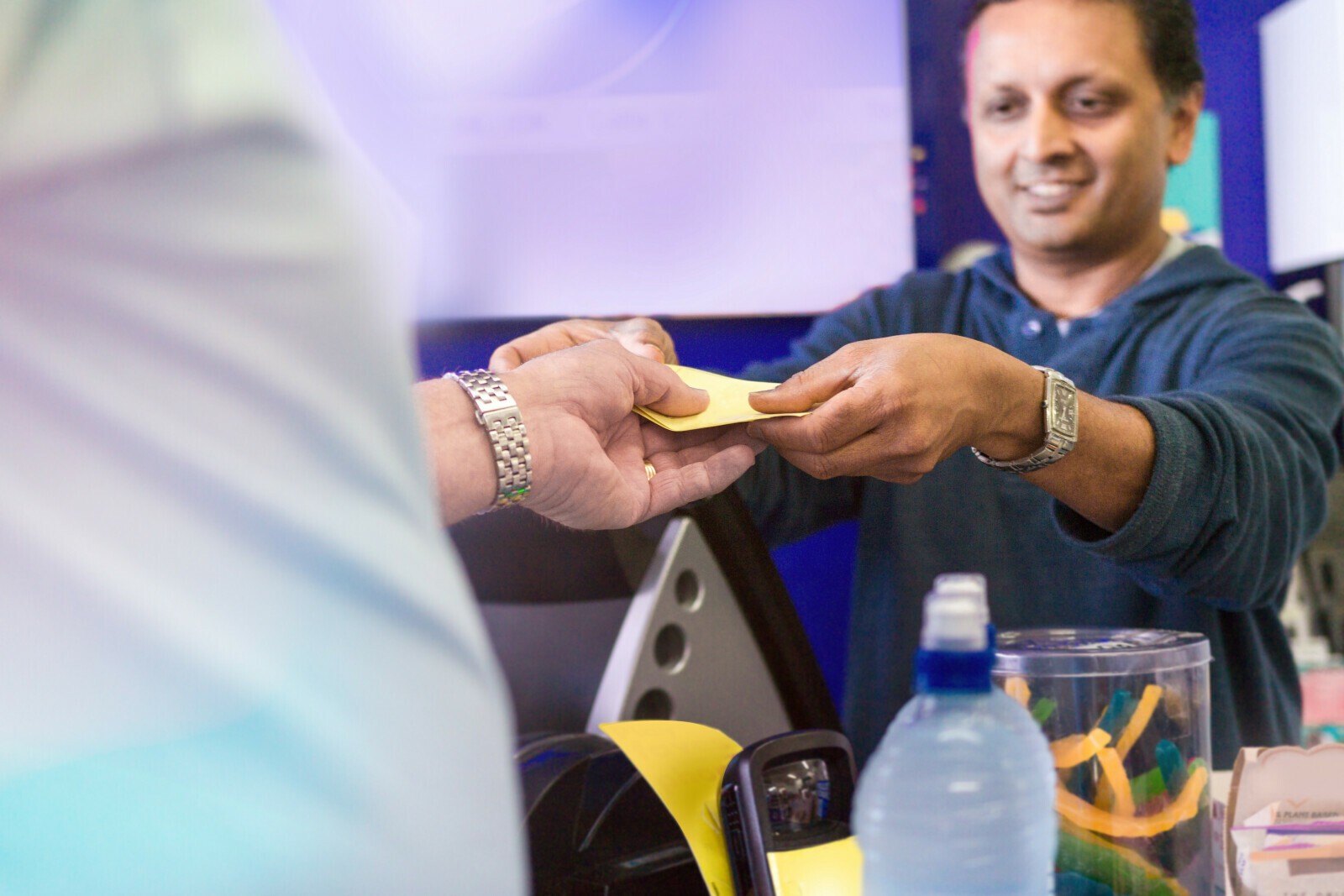 A New Zealand dairy owner handing change to a customer across the counter
